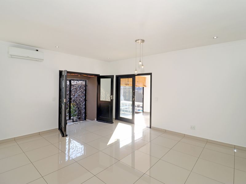 A bright, spacious living area featuring polished tiled floors, recessed lighting, a split-system air conditioner, and direct access to an outdoor patio area.