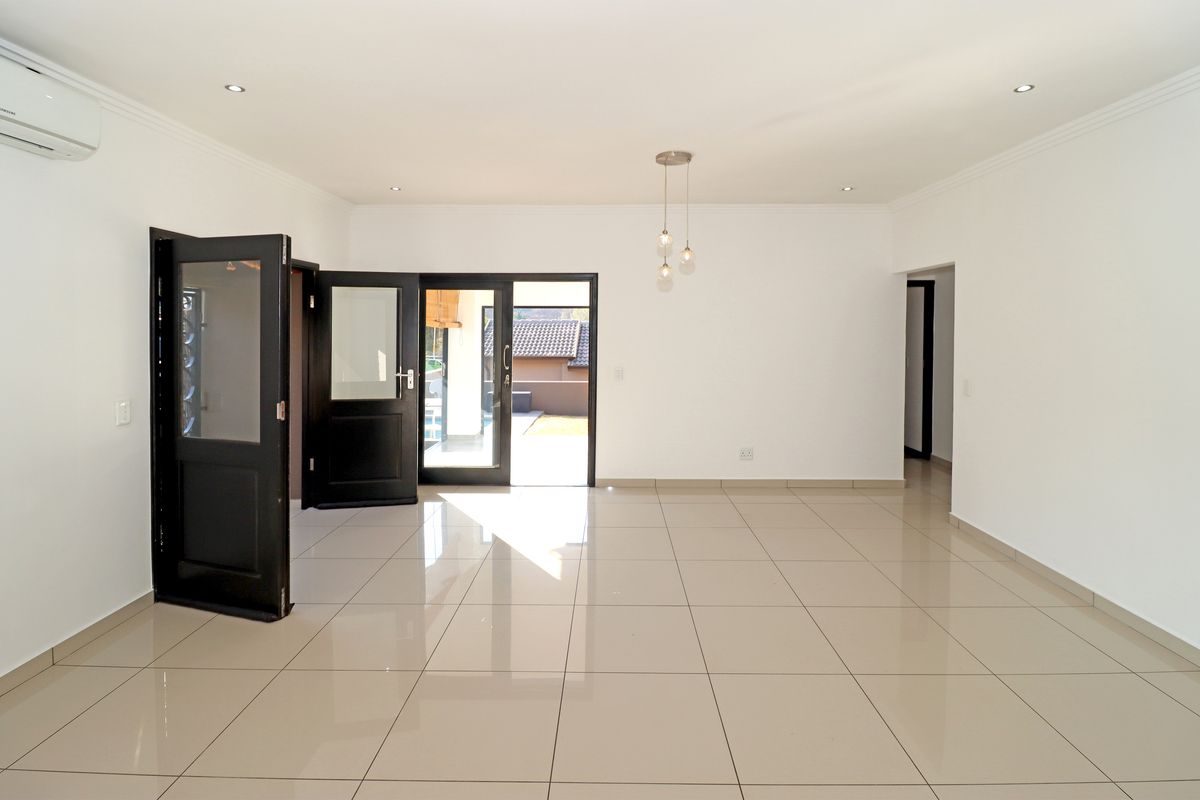 A bright, open-plan living area featuring polished porcelain floor tiles, recessed lighting, and direct access to the outdoor patio through double glass doors.