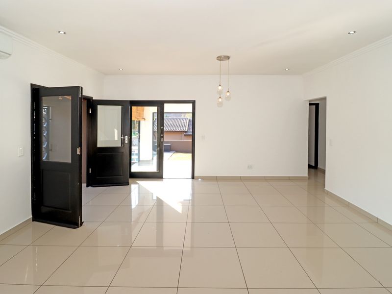 A bright, open-plan living area featuring polished porcelain floor tiles, recessed lighting, and direct access to the outdoor patio through double glass doors.