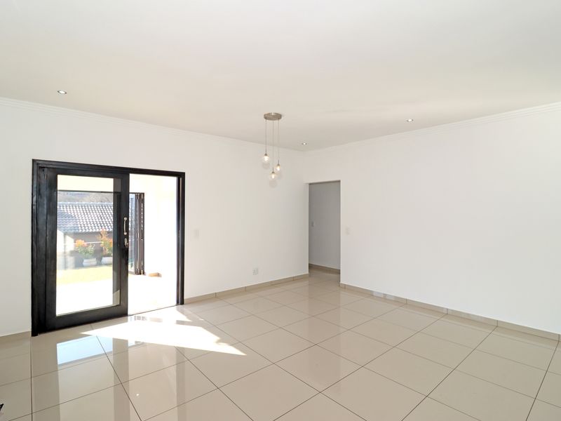 A bright, empty living area featuring neutral tiled flooring, recessed downlights, and a sliding glass door providing access to the outdoor space.