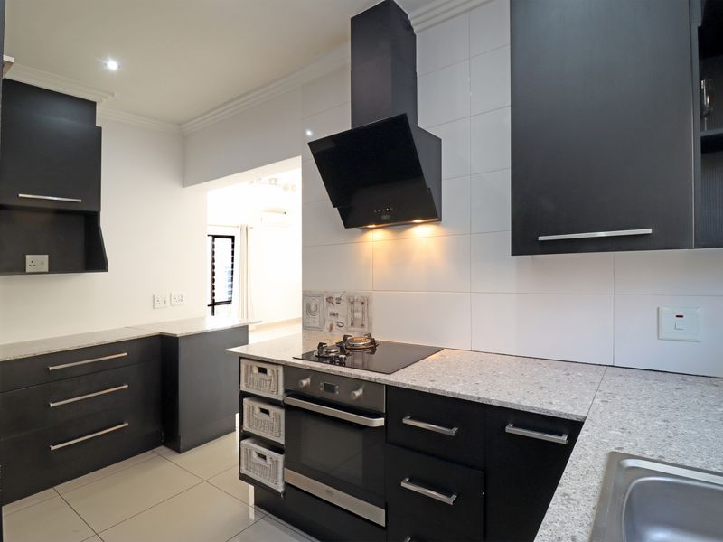 Modern kitchen featuring dark cabinetry, granite countertops, built-in oven, hob, extractor fan, and tiled finishes.