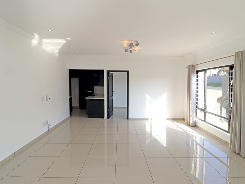 Spacious open-plan living area featuring neutral tiled flooring, recessed lighting, and large windows, leading into a modern kitchen space.
