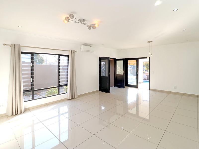 A bright, spacious, and empty living area featuring polished porcelain floor tiles, recessed lighting, and direct access to the outdoor patio area.