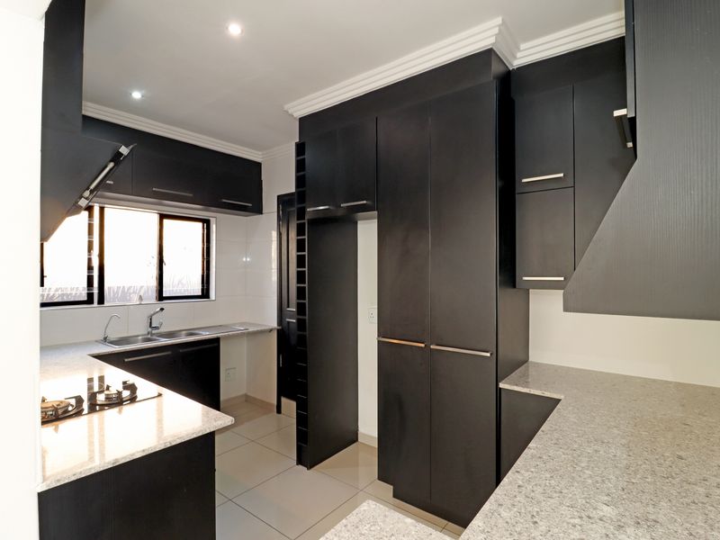 Modern kitchen featuring dark cabinetry, granite countertops, a gas hob, and tiled flooring. The space is clean, well-lit, and ready for use.