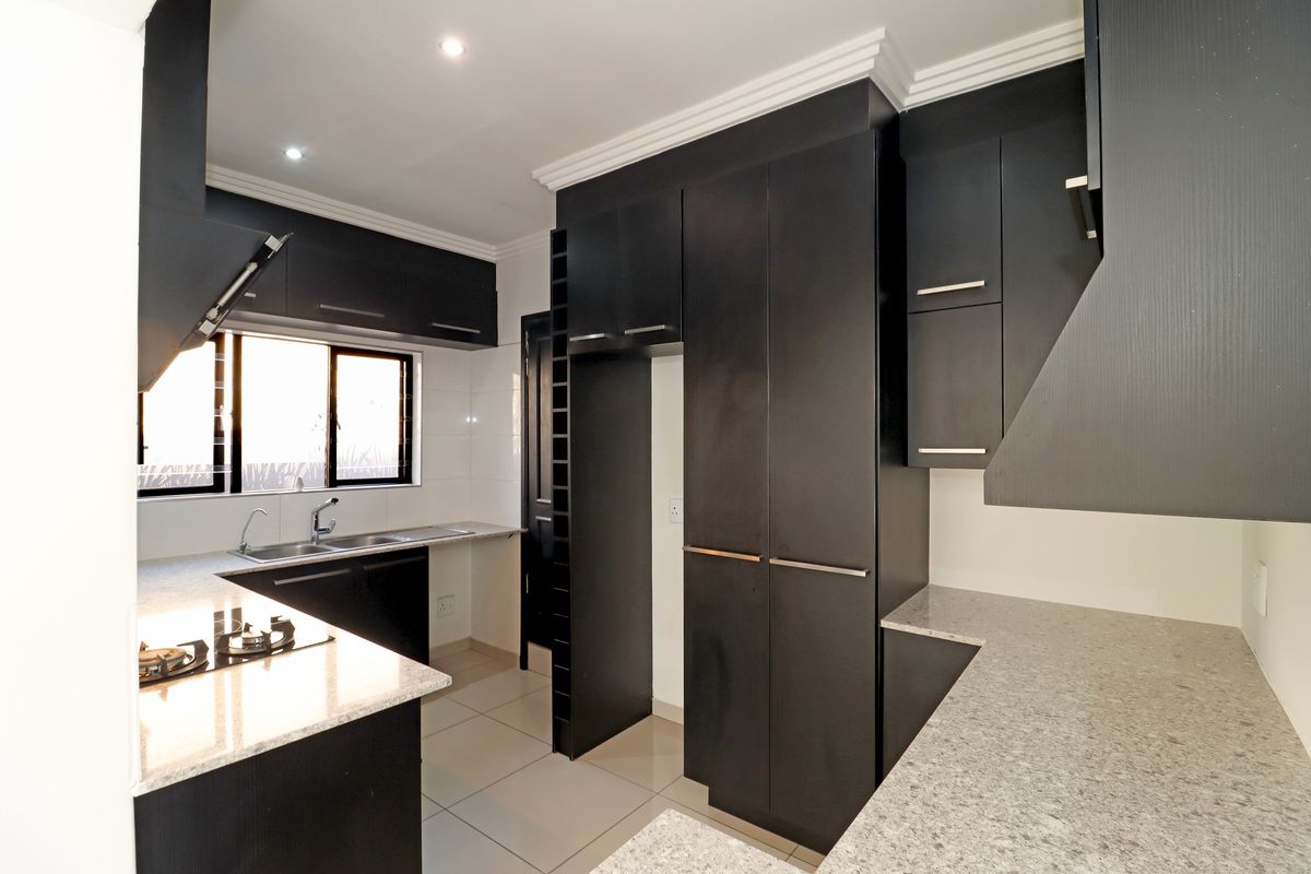 Modern kitchen featuring dark cabinetry, granite countertops, a gas hob, and tiled flooring. The space is clean, well-lit, and ready for use.