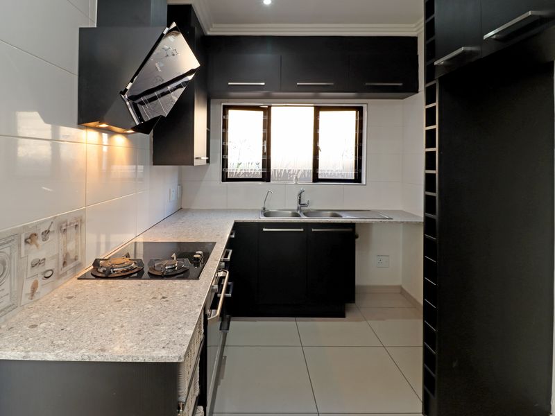 Modern kitchen featuring sleek black cabinetry, granite countertops, a built-in hob with extractor fan, and a stainless steel double sink.