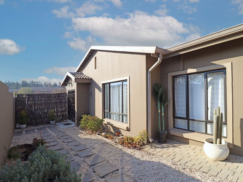 A well-maintained rear exterior view featuring a paved walkway, gravel landscaping, and modern aluminium window frames set against a neutral-toned facade.