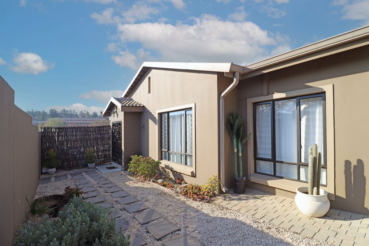 A well-maintained rear exterior view featuring a paved walkway, gravel landscaping, and modern aluminium window frames set against a neutral-toned facade.