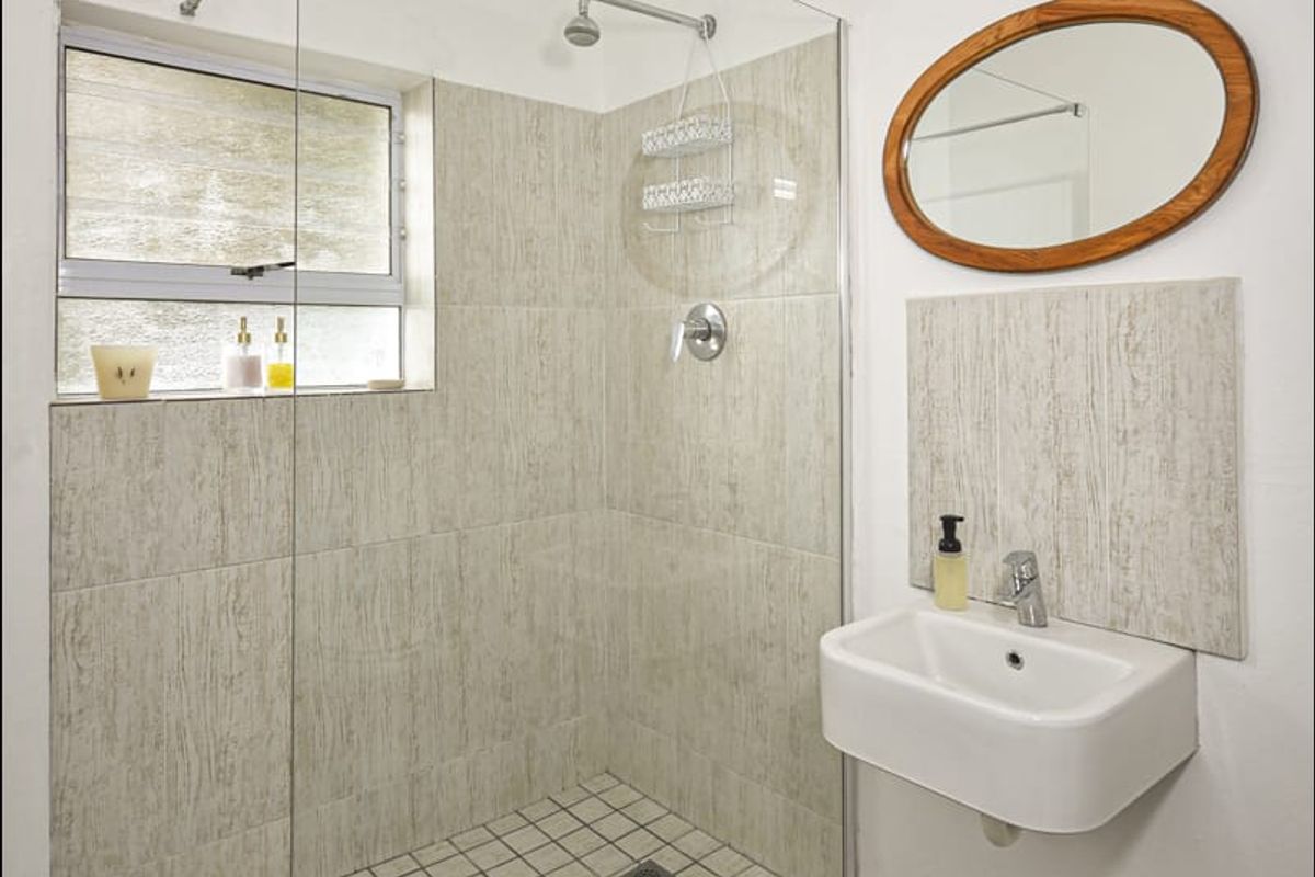 A functional bathroom featuring a walk-in shower with glass enclosure, wall-mounted basin, and neutral tiled finishes.