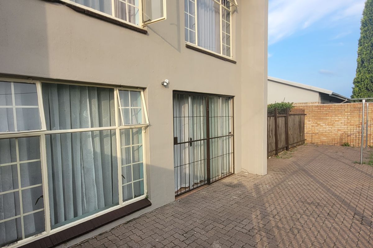 Rear exterior view of the townhouse featuring a paved patio area, security gates, and perimeter fencing.
