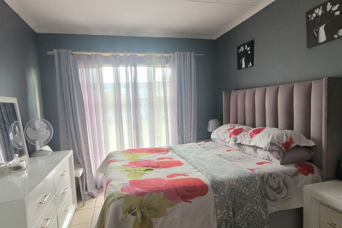 A well-lit bedroom featuring tiled flooring and large windows with curtain rails, providing a comfortable and functional living space.