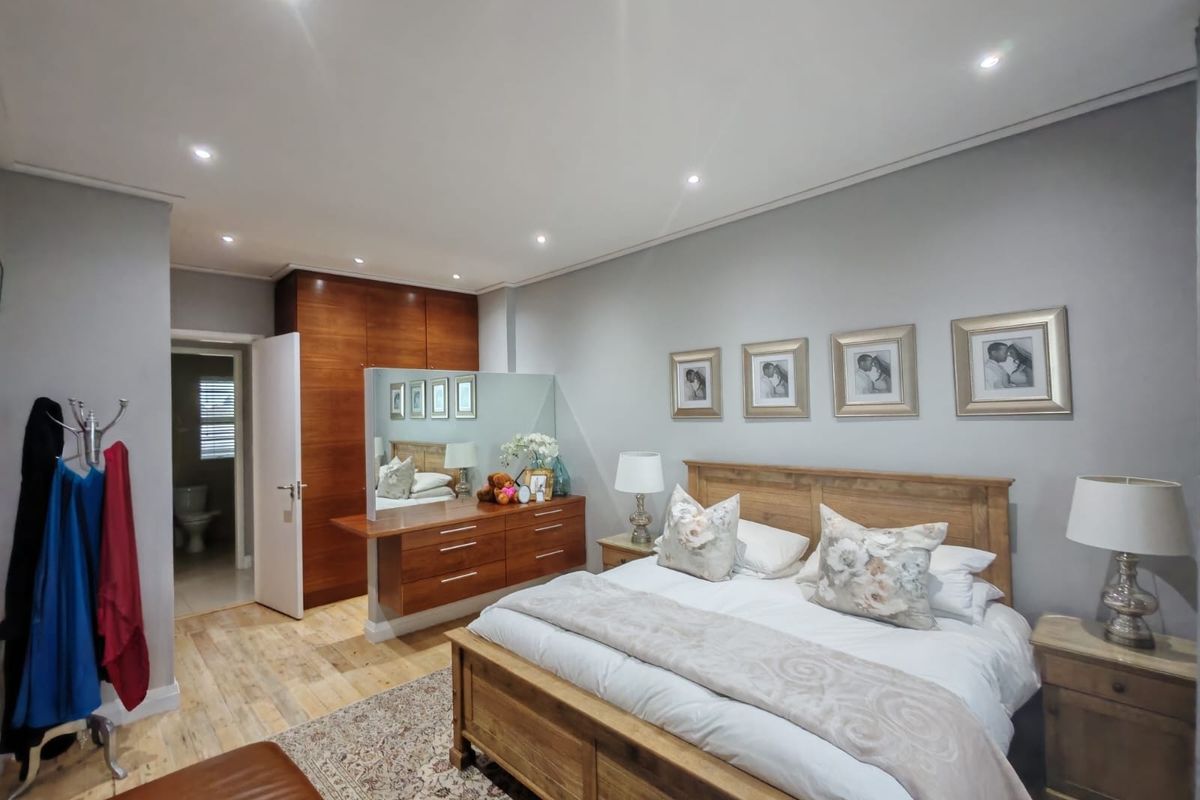 Spacious bedroom featuring warm wooden flooring, built-in cabinetry, recessed lighting, and direct access to an en-suite bathroom.