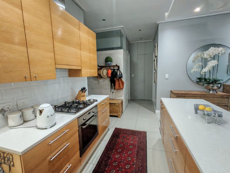 Modern kitchen featuring light wood cabinetry, stone countertops, a gas hob, built-in oven, and a central island with tiled flooring.