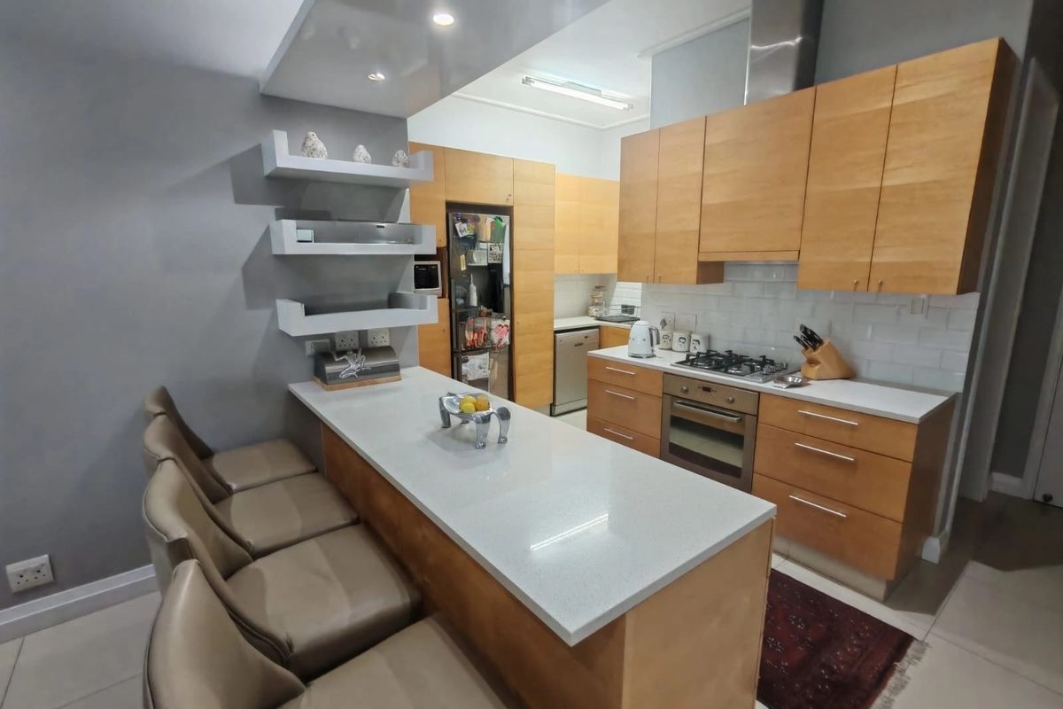 Modern kitchen featuring light wood cabinetry, stone countertops, a breakfast bar, gas hob, and integrated stainless steel appliances.