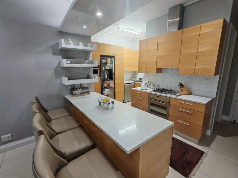 Modern kitchen featuring light wood cabinetry, stone countertops, a breakfast bar, gas hob, and integrated stainless steel appliances.