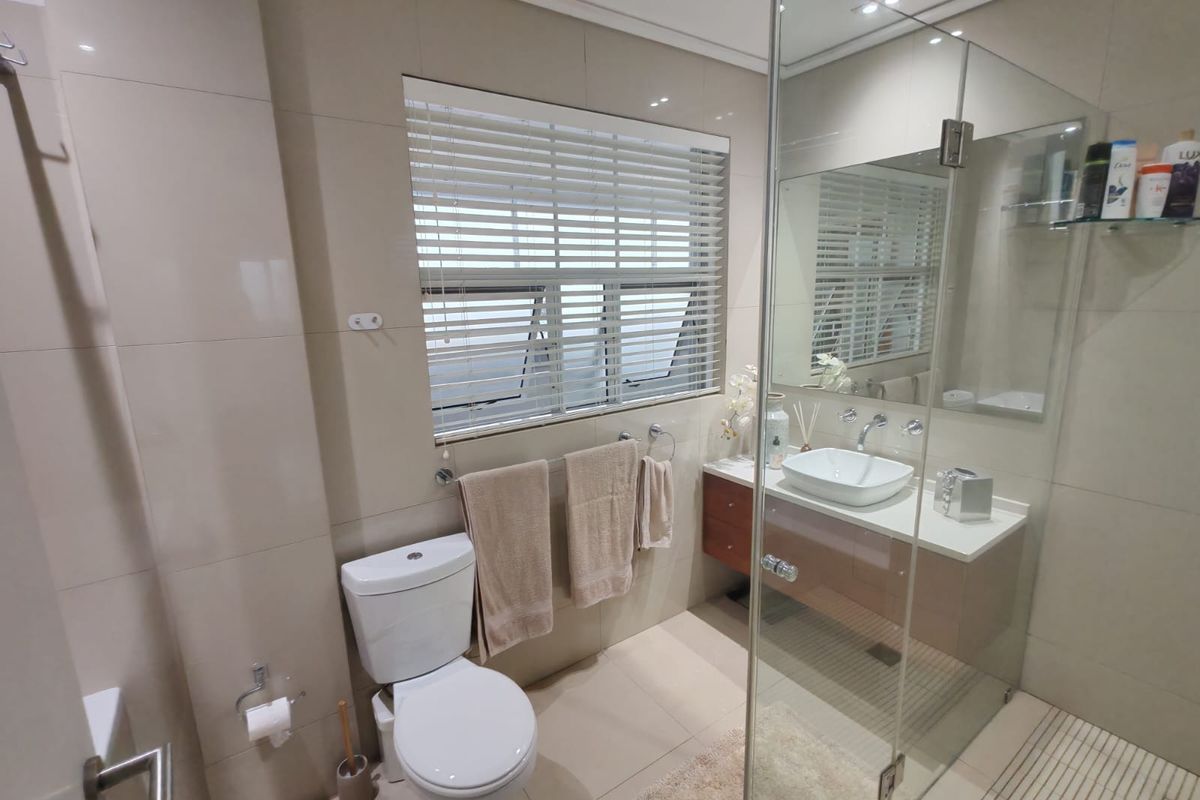 Modern bathroom featuring a wall-mounted toilet, a sleek vanity with a vessel sink, and a spacious glass-enclosed shower with tiled finishes.