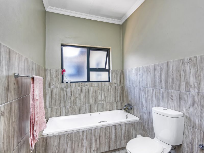 A clean bathroom featuring a built-in bathtub with wood-look tile surround, a standard toilet, and a frosted glass window for privacy.