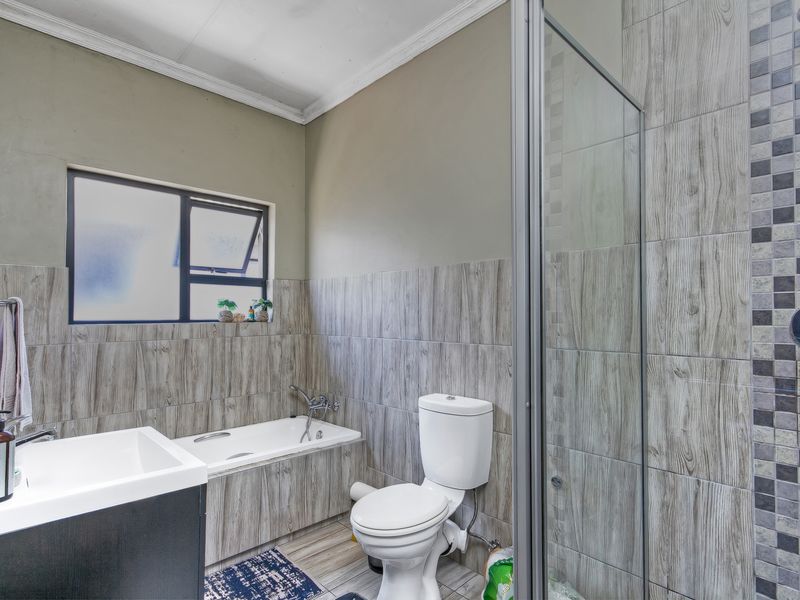 A functional bathroom featuring a built-in bathtub, separate shower enclosure, toilet, and vanity basin with modern wood-look wall tiling.