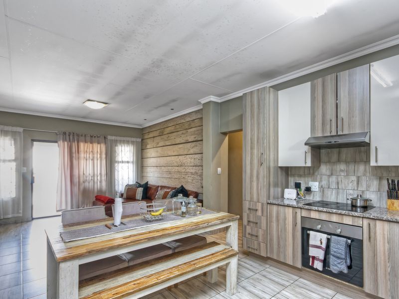 Open-plan living and kitchen area featuring modern wood-look cabinetry, built-in appliances, tiled flooring, and direct access to an outdoor space.