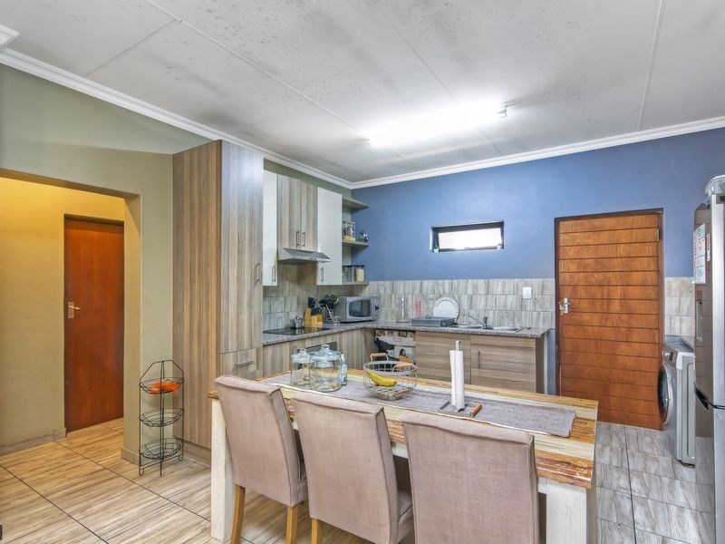 Open-plan kitchen and dining area featuring wood-look cabinetry, tiled flooring, and direct access to adjacent rooms.