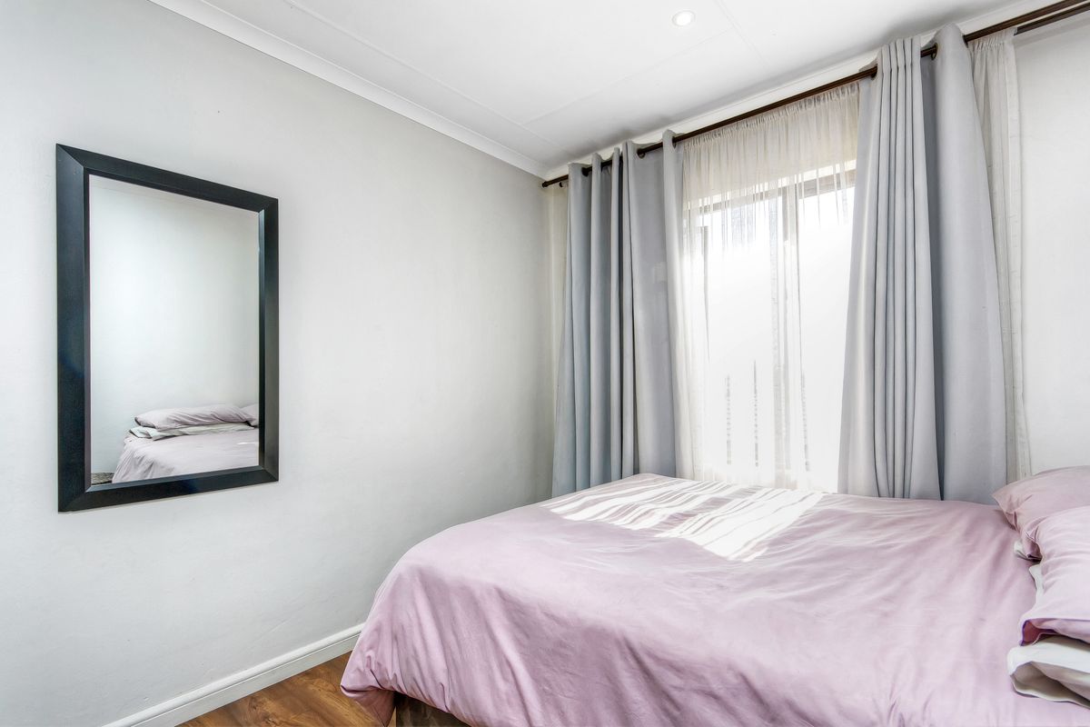 A well-maintained bedroom featuring laminate flooring, neutral wall finishes, and a window dressed with curtains, providing a bright and comfortable living space.