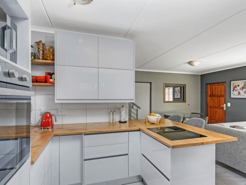 Modern open-plan kitchen featuring sleek gloss cabinetry, wood-look laminate countertops, built-in appliances, and a seamless flow into the adjacent living area.