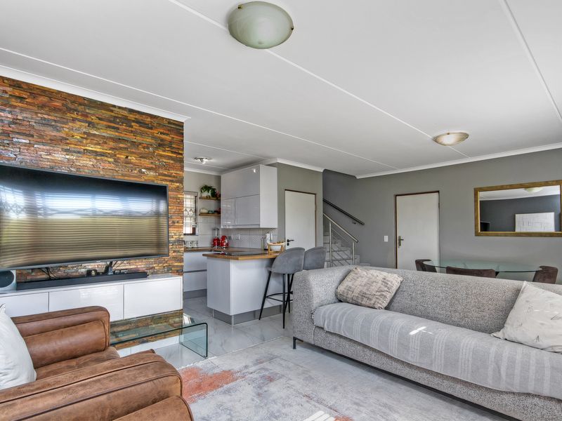 Open-plan living area featuring a striking stacked stone feature wall, modern kitchen cabinetry with wooden countertops, and a staircase with metal balustrades.