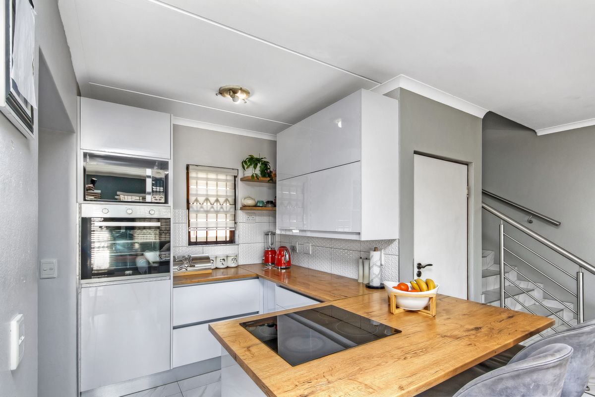 Modern kitchen featuring white cabinetry, wooden countertops, built-in oven and microwave, and a breakfast bar, adjacent to a staircase with metal balustrades.