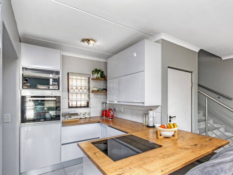 Modern kitchen featuring white cabinetry, wooden countertops, built-in oven and microwave, and a breakfast bar, adjacent to a staircase with metal balustrades.