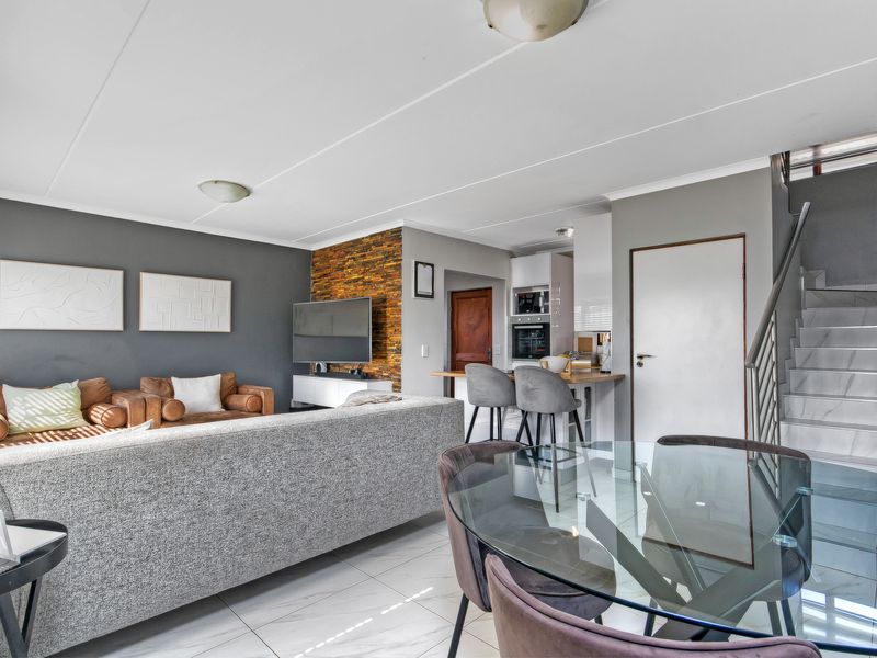 Open-plan living and dining area featuring a modern kitchen with built-in appliances, a stone feature wall, and a staircase leading to the upper level.