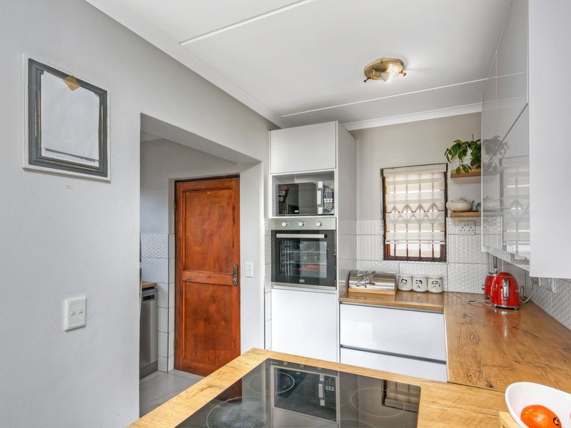 Modern kitchen featuring sleek white cabinetry, wooden countertops, built-in oven and microwave, and a tiled backsplash, with an adjacent utility area.
