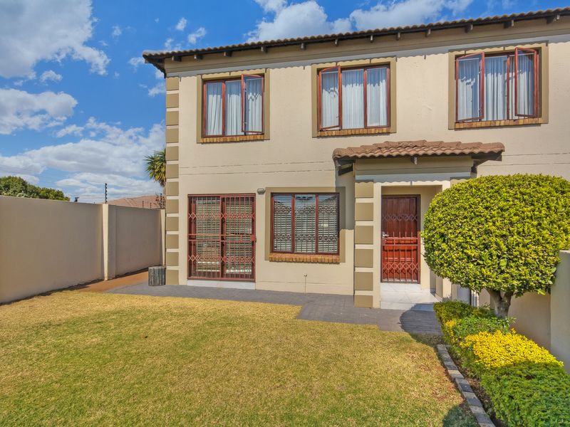 Rear view of a double-story townhouse featuring a private garden, paved walkway, security gates, and perimeter boundary wall with electric fencing.