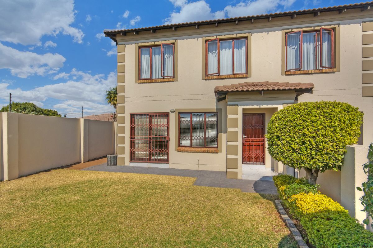 Rear view of a double-story townhouse featuring a private garden, paved walkway, security gates, and perimeter boundary wall with electric fencing.