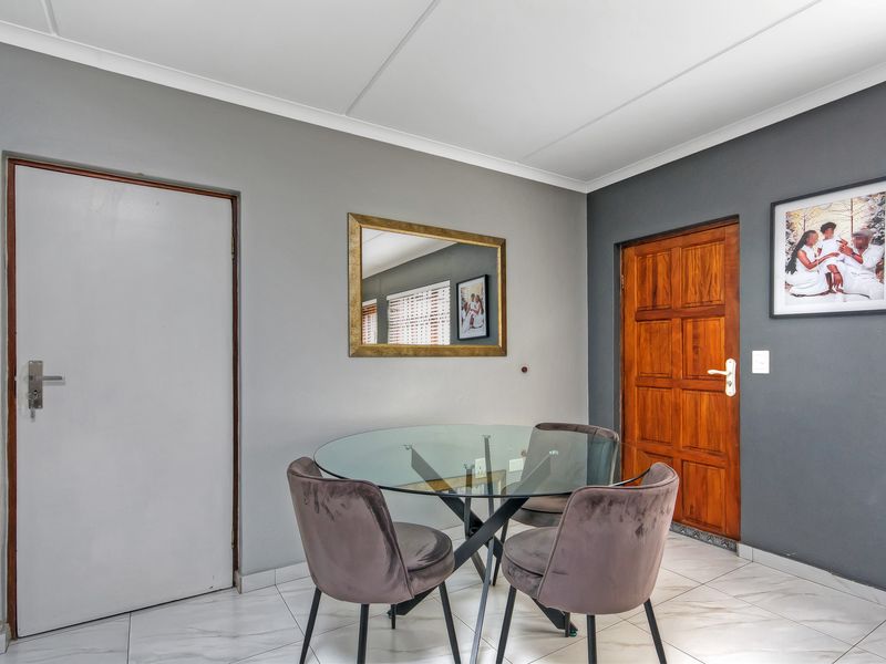 A well-maintained dining area featuring neutral grey walls, tiled flooring, and a classic timber panel door.
