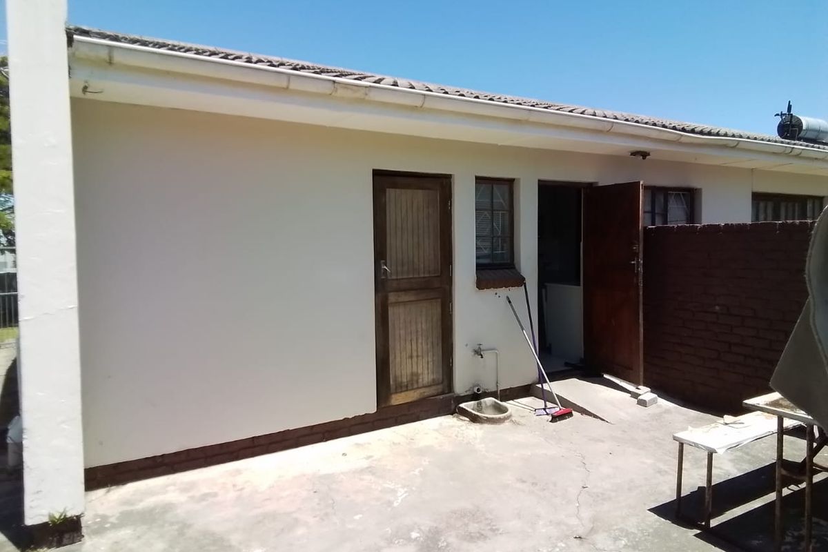 Rear exterior view of the house featuring a concrete patio area, brick walling, and access doors to the utility or service area.