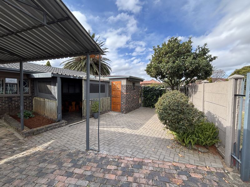 Rear exterior area featuring a paved courtyard, covered carport, and brick-built structure with a patio space.