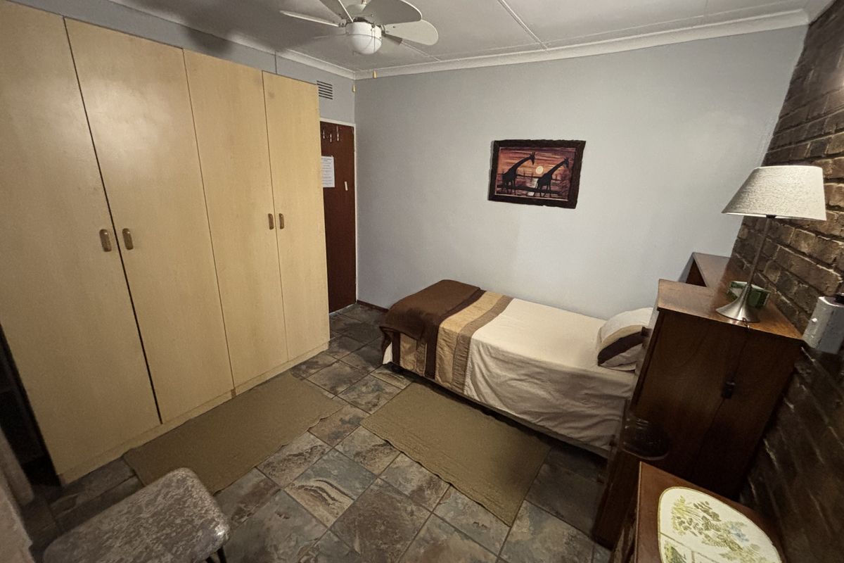 A bedroom featuring built-in cupboards, a ceiling fan, tiled flooring, and an exposed brick feature wall.