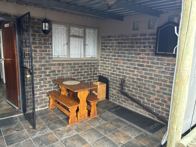 A covered patio area featuring exposed brick walls, tiled flooring, and a security gate, providing a functional outdoor space for relaxation.