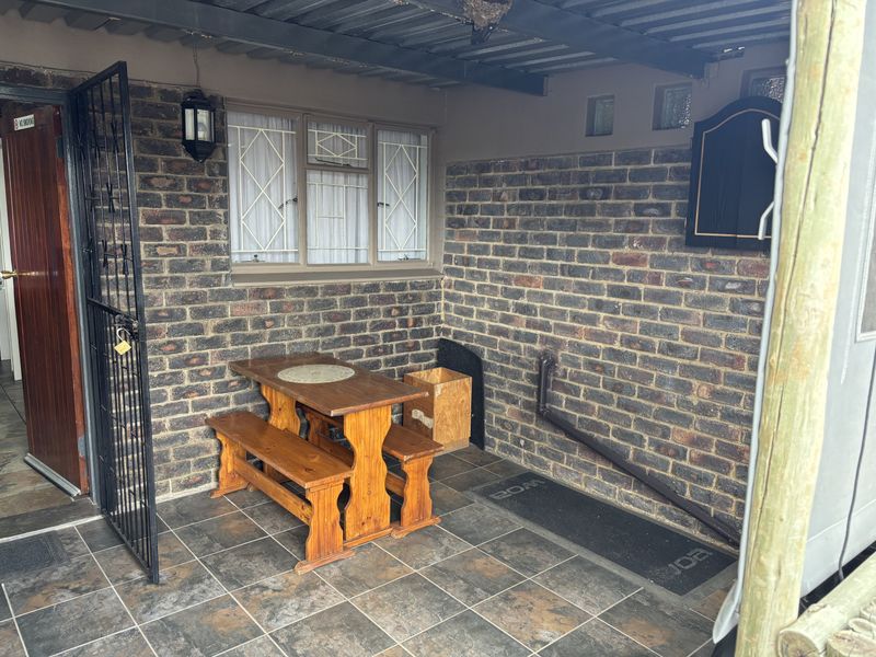 A covered patio area featuring exposed brick walls, tiled flooring, and a secure metal gate, providing a functional outdoor space.
