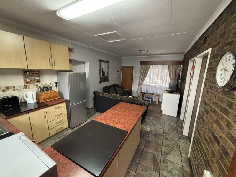 Open-plan living and kitchen area featuring tiled flooring, exposed brick wall, and functional built-in cabinetry with laminate countertops.