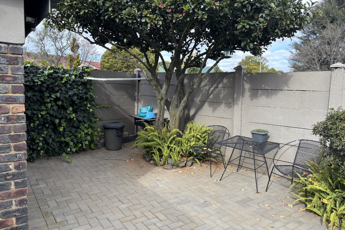 A private rear courtyard featuring paved flooring, a mature tree, and a secure precast concrete boundary wall.
