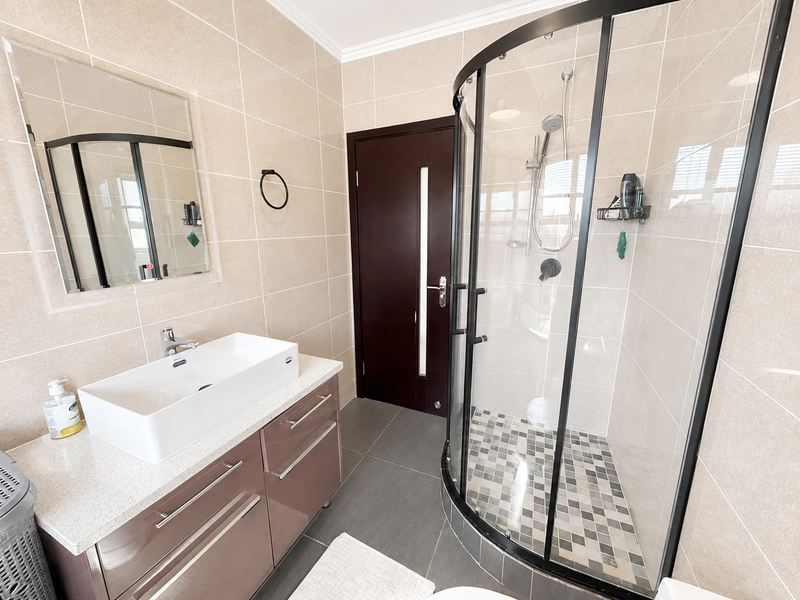 Modern bathroom featuring a vessel sink vanity, a curved glass shower enclosure with mosaic floor tiling, and neutral wall tiles.