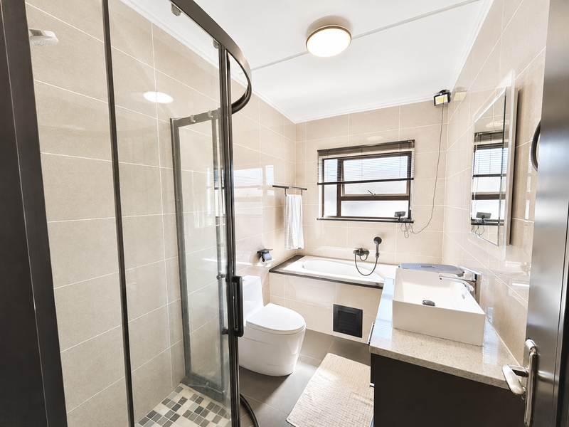 Modern bathroom featuring a glass shower enclosure, built-in bathtub, contemporary vanity basin with stone countertop, and neutral floor-to-ceiling wall tiling.