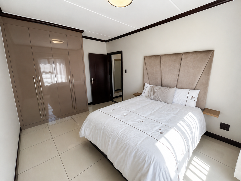 A well-maintained bedroom featuring large format floor tiles, a high-gloss built-in wardrobe, and a neutral color palette.