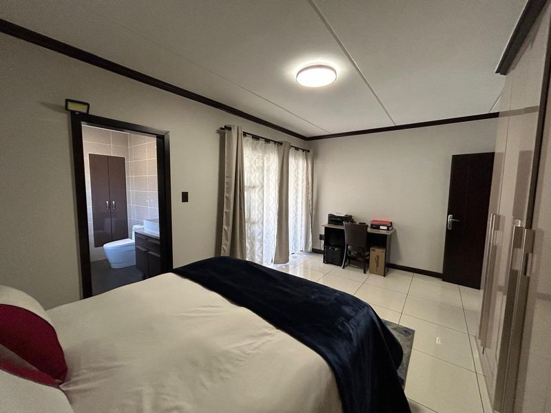 Spacious bedroom featuring tiled flooring, a built-in wardrobe, and direct access to an en-suite bathroom and outdoor area through sliding glass doors.