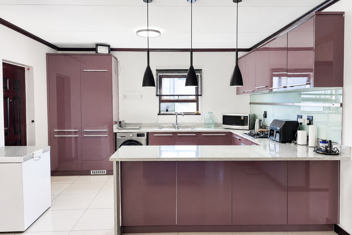 Modern kitchen featuring high-gloss cabinetry, stone countertops, integrated appliances, glass splashback, and stylish pendant lighting in an open-plan layout.