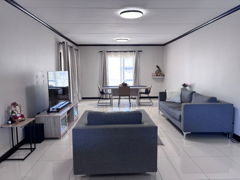 A bright open-plan living and dining area featuring large format floor tiles, modern ceiling lighting, and a sliding glass door providing natural light.