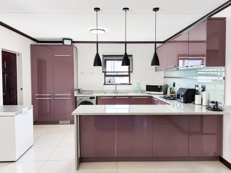 Modern kitchen featuring high-gloss cabinetry, stone countertops, integrated appliances, glass splashback, and stylish pendant lighting in an open-plan layout.