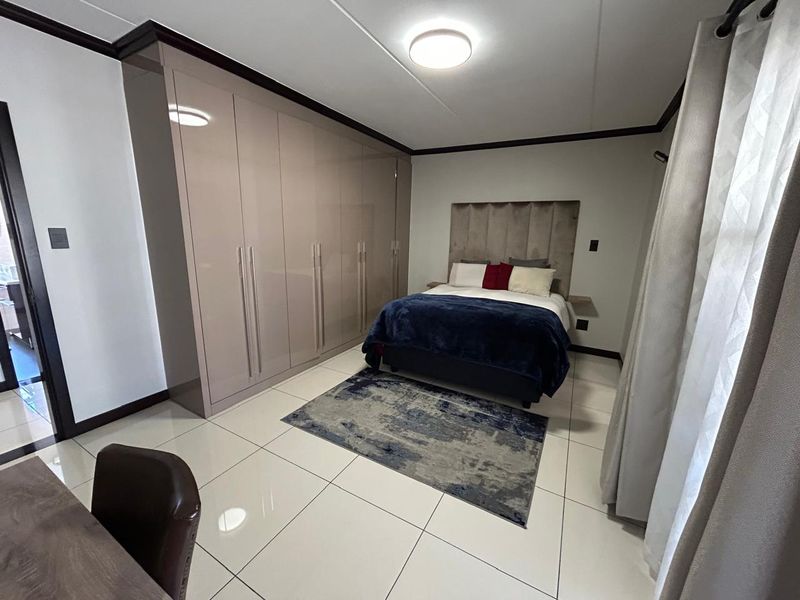A well-maintained bedroom featuring high-gloss built-in cupboards, polished tile flooring, and modern ceiling lighting, offering a clean and contemporary living space.