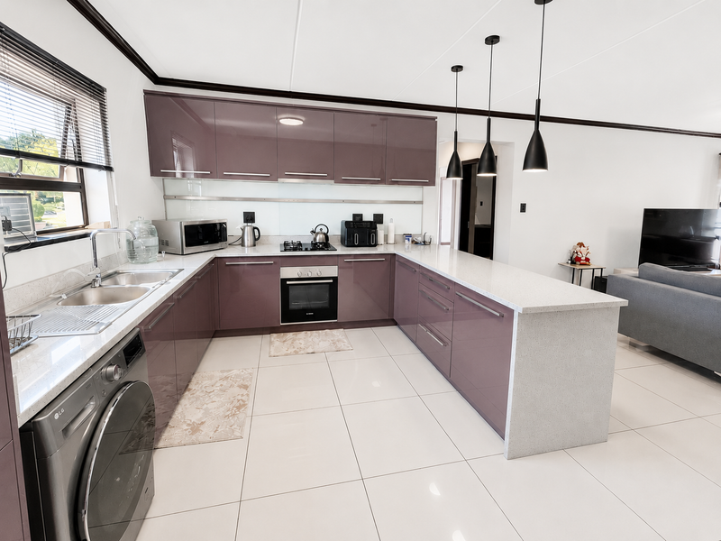 Modern open-plan kitchen featuring high-gloss purple cabinetry, stone countertops, integrated appliances, and sleek pendant lighting, seamlessly flowing into the adjacent living area.
